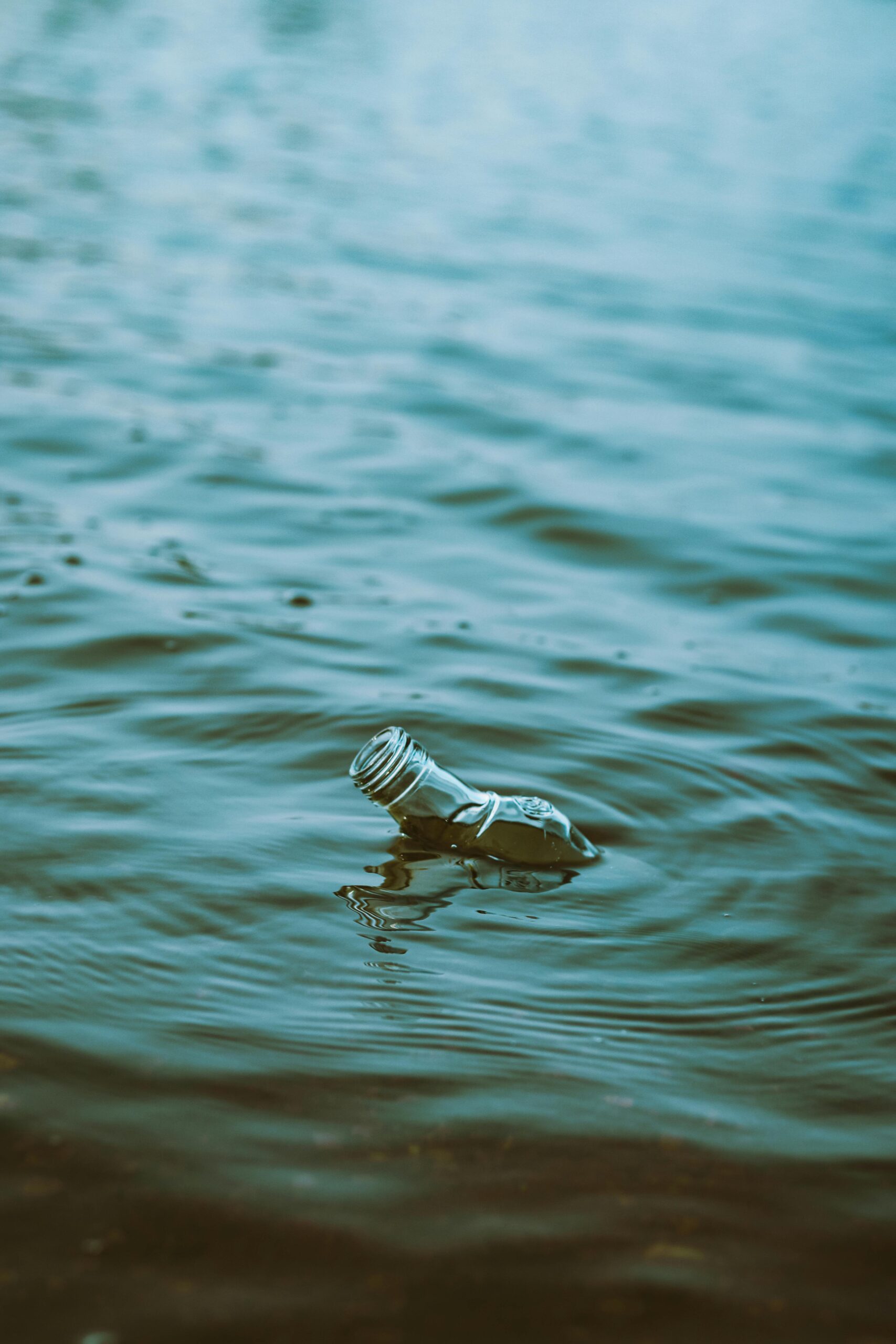 A glass bottle floats in water creating ripples, illustrating pollution and environmental impact.